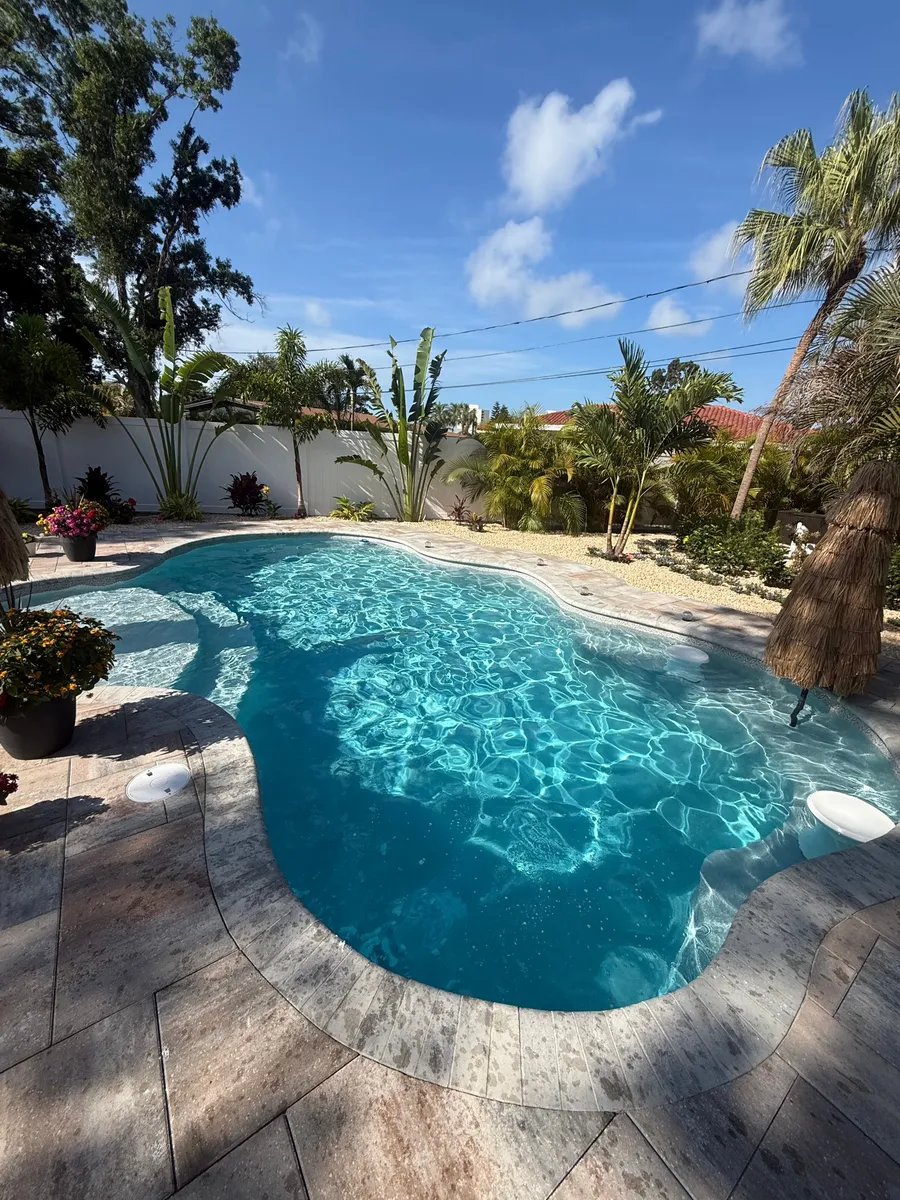 Clear blue backyard pool with palm trees and paver deck